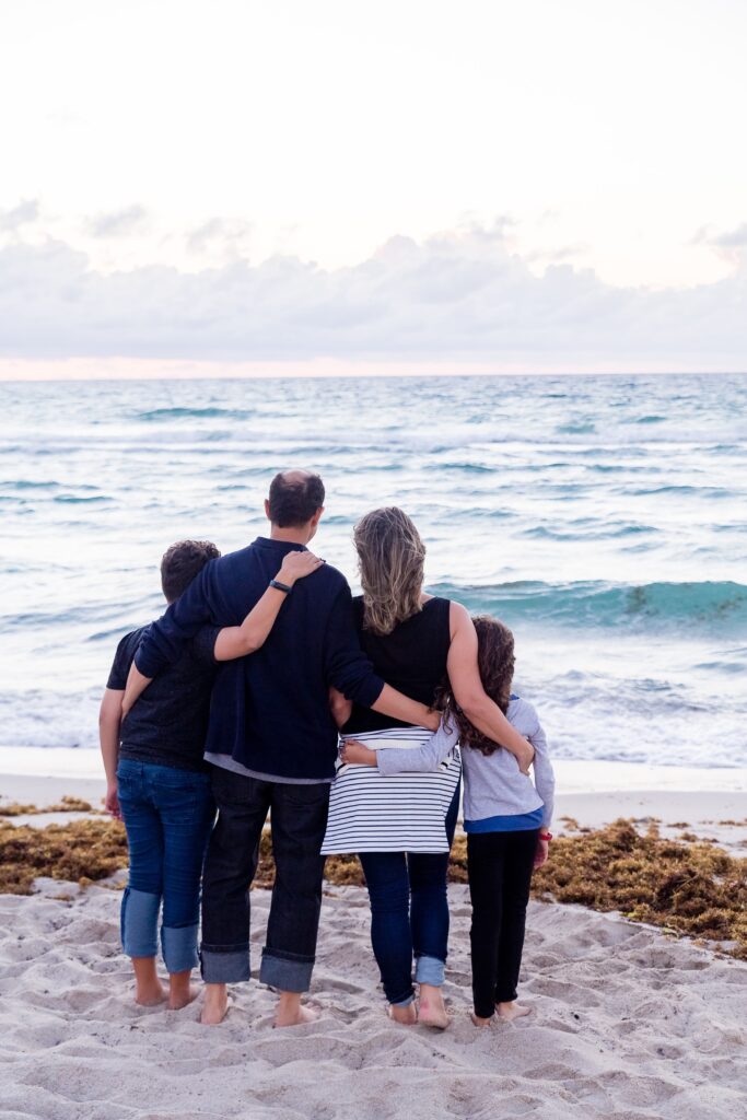 Family standing together on the beach, embracing each other while gazing at the ocean, symbolizing connection and support in family therapy.