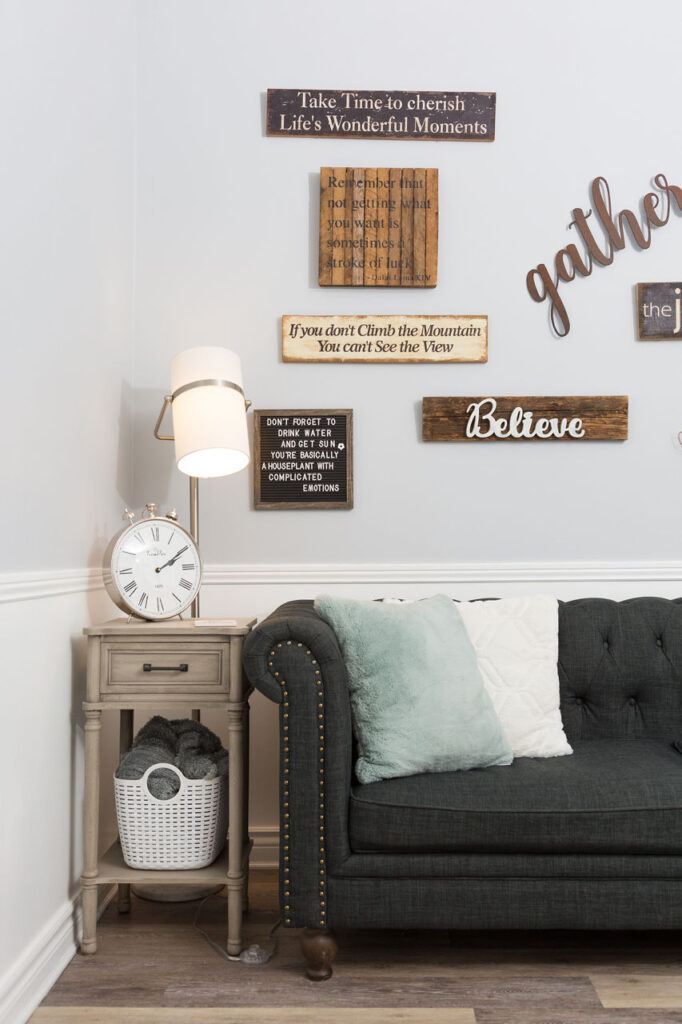 Cozy living room corner featuring a dark gray tufted sofa with decorative pillows, a side table with a clock, and motivational wall art promoting self-worth and mindfulness.
