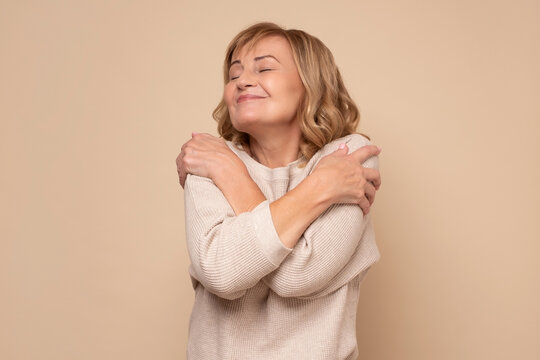 Woman in a cozy sweater embracing herself, symbolizing self-love and self-compassion, against a neutral background, relevant to themes of overcoming negative self-talk and nurturing self-worth.