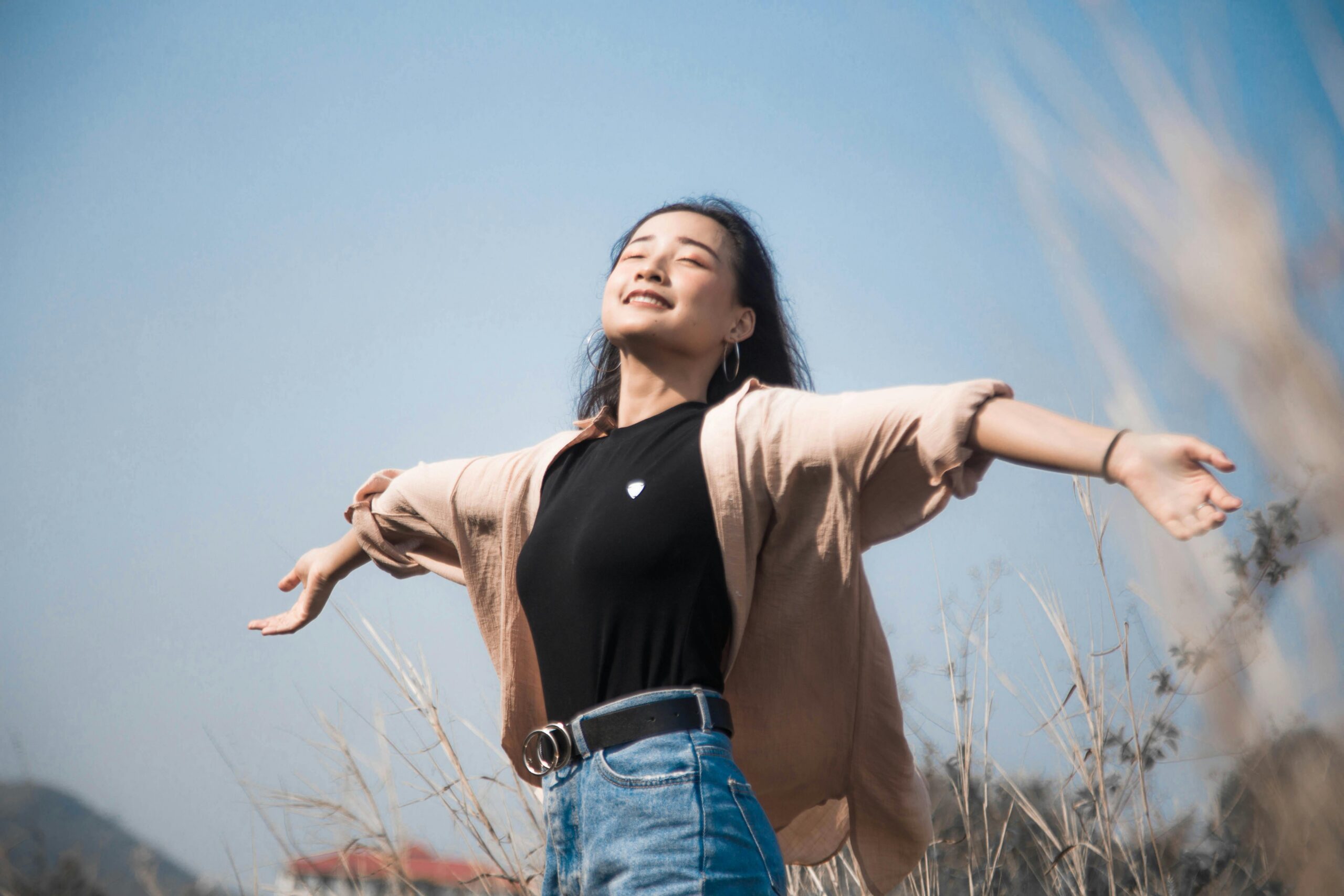 Person with outstretched arms in a natural setting, embodying mindfulness and freedom, against a clear blue sky, representing mental well-being and holistic practices.