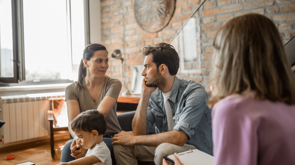 Family mediation session with a couple and child, discussing separation and divorce, in a warm, inviting therapy setting.