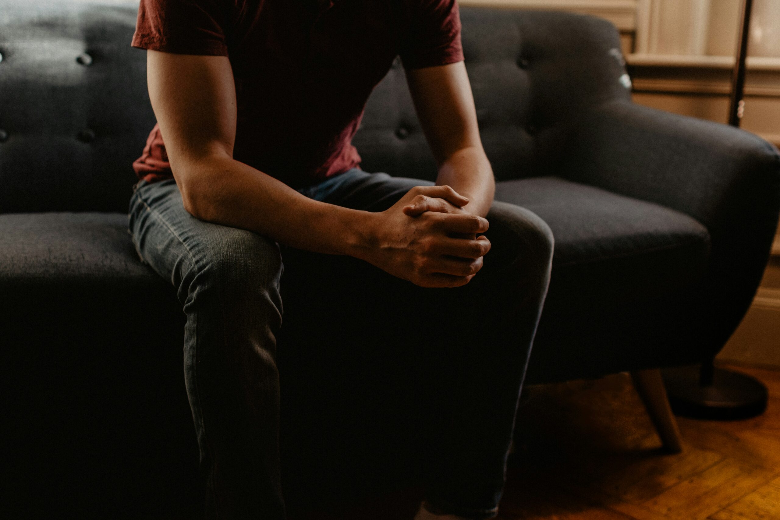 Person sitting on a couch with hands clasped, reflecting contemplation and emotional support, relevant to therapy services including anxiety and grief at Balanced Life Therapy.