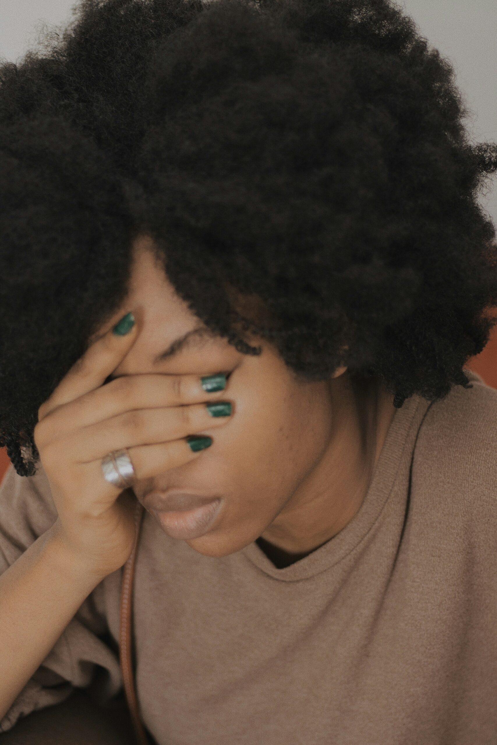 Person with natural hair and green nails covering face, representing teen emotional challenges and support.