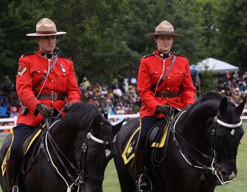 Police officers, including two mounted officers on horseback, stand on a wet city street beside a police SUV in front of a commercial building with a Sleep Country store entrance.